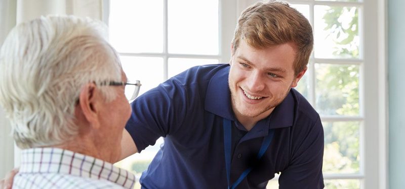 A carer supporting an older man by a window